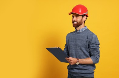 Photo of Professional engineer in hard hat with clipboard on yellow background, space for text