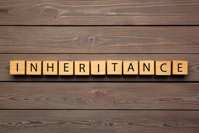 Photo of Word Inheritance made with cubes on wooden background, flat lay