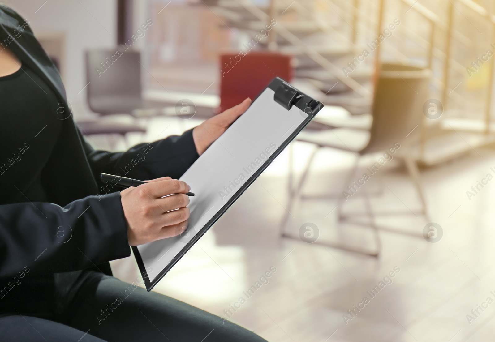 Photo of Psychologist with clipboard prepared for group therapy on blurred background, closeup. Space for text