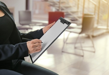 Psychologist with clipboard prepared for group therapy on blurred background, closeup. Space for text