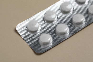 Photo of White pills in blister on beige background, closeup