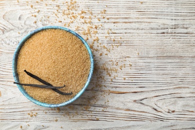 Photo of Bowl with brown vanilla sugar on wooden background, top view