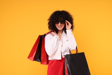 Photo of Happy young woman with shopping bags and stylish sunglasses on yellow background