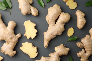 Photo of Fresh ginger with green leaves on dark background, flat lay