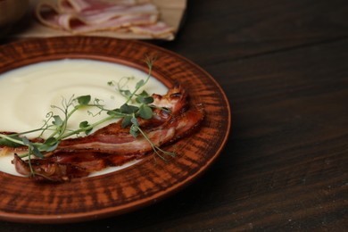 Delicious potato soup with bacon and microgreens in bowl on wooden table, closeup. Space for text