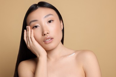 Photo of Beautiful young Asian woman applying body cream on shoulder against beige background