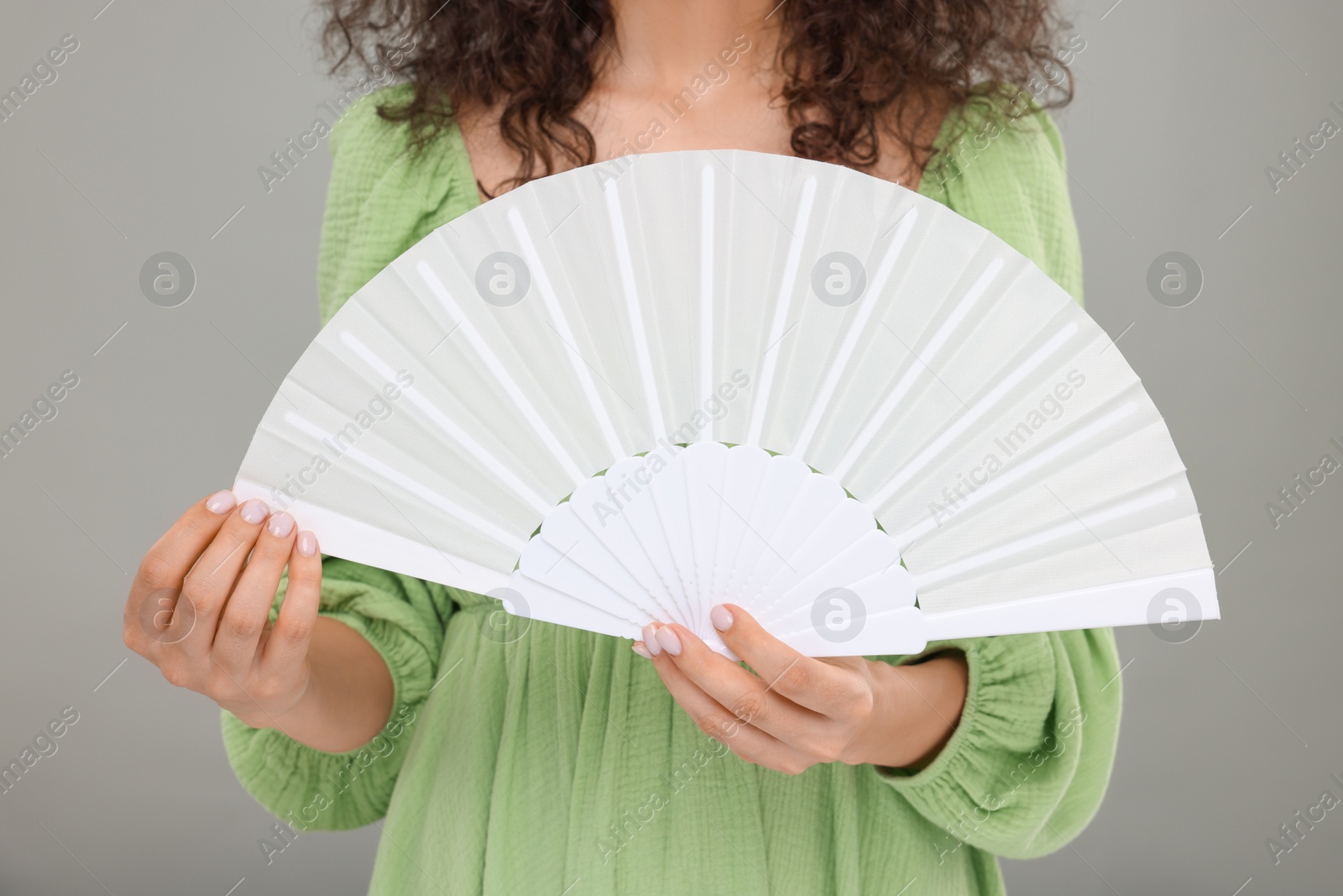 Photo of Woman holding hand fan on light grey background, closeup