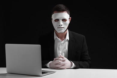 Photo of Man in mask and gloves sitting with laptop at white table against black background