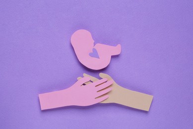 Photo of Woman`s health. Hands with newborn paper figures on lilac background, flat lay