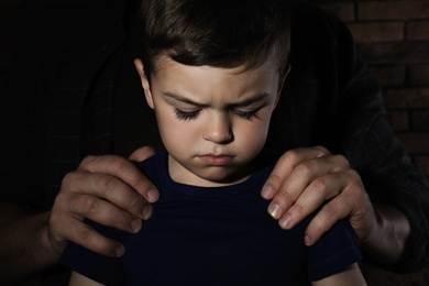 Photo of Despaired little boy and adult man on dark background. Child in danger