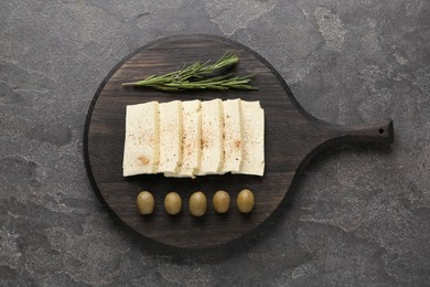 Photo of Cut tofu with olives and rosemary on grey table, top view. Soya bean curd