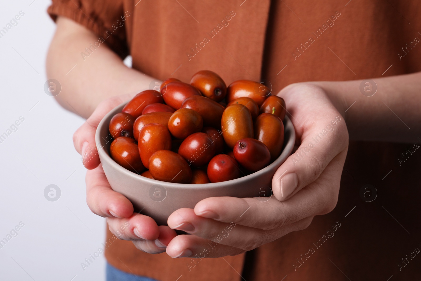 Photo of Woman holding bowl with fresh Ziziphus jujuba fruits on light background, closeup