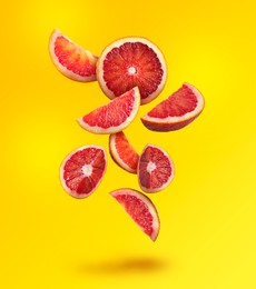 Cut tasty Sicilian oranges falling on yellow background