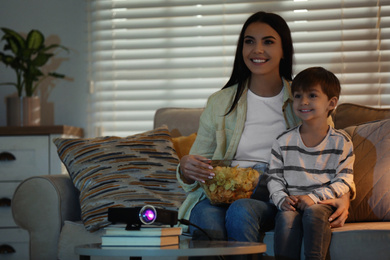 Photo of Young woman and her son watching movie using video projector at home. Space for text