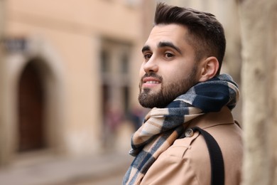 Photo of Smiling man in warm scarf on city street. Space for text