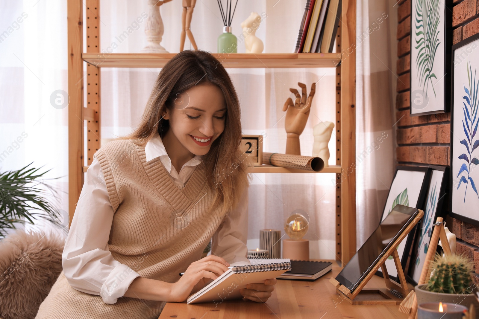 Photo of Young woman drawing in sketchbook with pencil at wooden table indoors