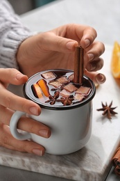 Photo of Woman holding mug with hot mulled wine on table, closeup