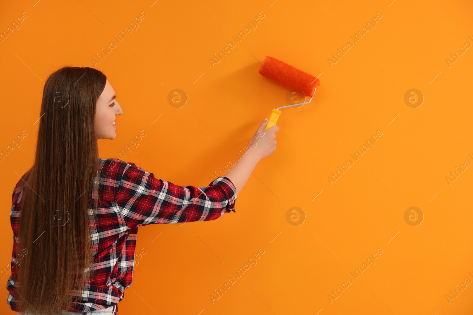 Photo of Designer painting orange wall with roller, space for text