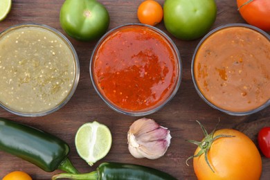Photo of Flat lay composition of tasty salsa sauces and different ingredients on wooden table