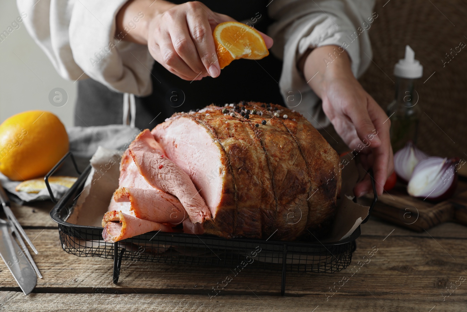 Photo of Woman squeezing juice from orange slice onto delicious baked ham at wooden table, closeup