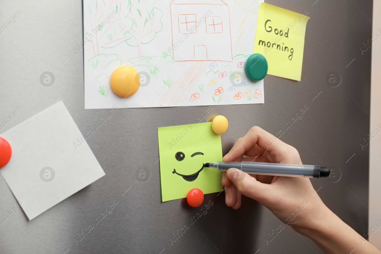 Photo of Woman drawing happy smile on note stuck to refrigerator door, closeup