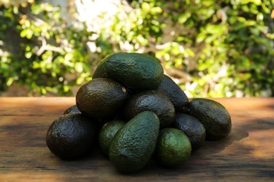 Photo of Pile of fresh avocados on wooden table outdoors, closeup