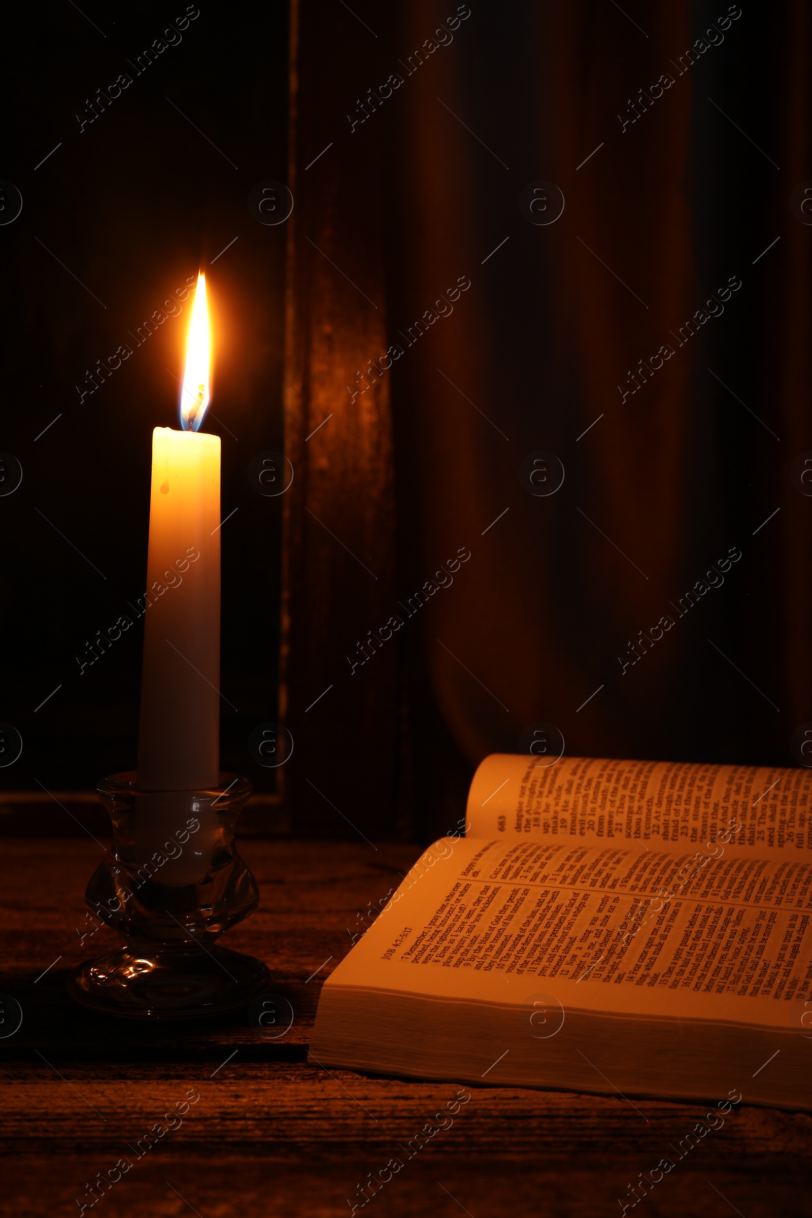 Photo of Burning candle and Bible on wooden table at night