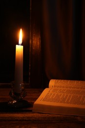 Photo of Burning candle and Bible on wooden table at night