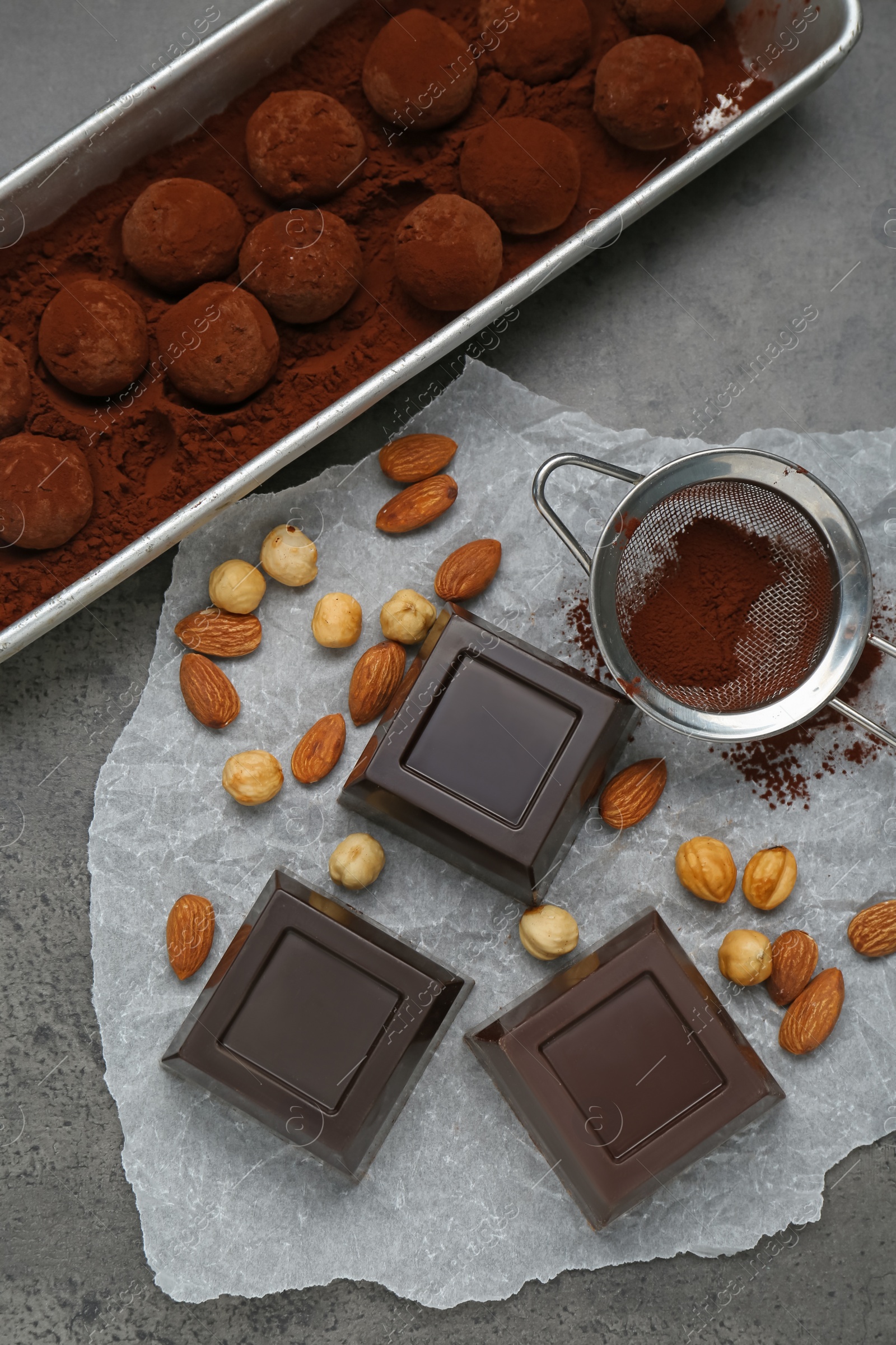 Photo of Delicious chocolate candies powdered with cocoa, sieve and ingredients on grey table, flat lay