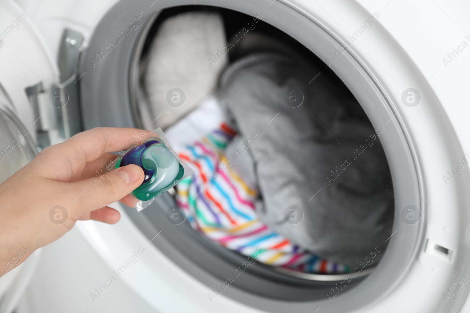 Photo of Woman putting laundry detergent capsule into washing machine, closeup