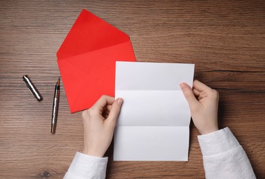 Photo of Woman with blank sheet of paper at wooden table, top view. Space for text