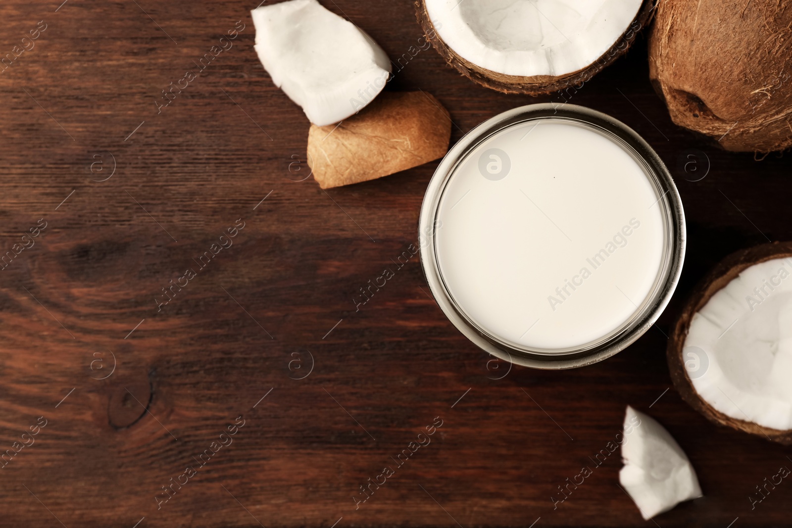 Photo of Glass of delicious vegan milk and coconut pieces on wooden table, flat lay. Space for text