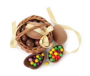 Photo of Wicker basket with tasty chocolate eggs and colorful candies on white background, top view