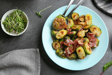 Delicious roasted Brussels sprouts with bacon served on black table, flat lay