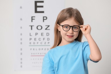 Photo of Little girl with glasses against vision test chart