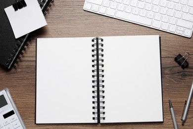 Photo of Open blank notebook, keyboard and stationery on wooden table, flat lay