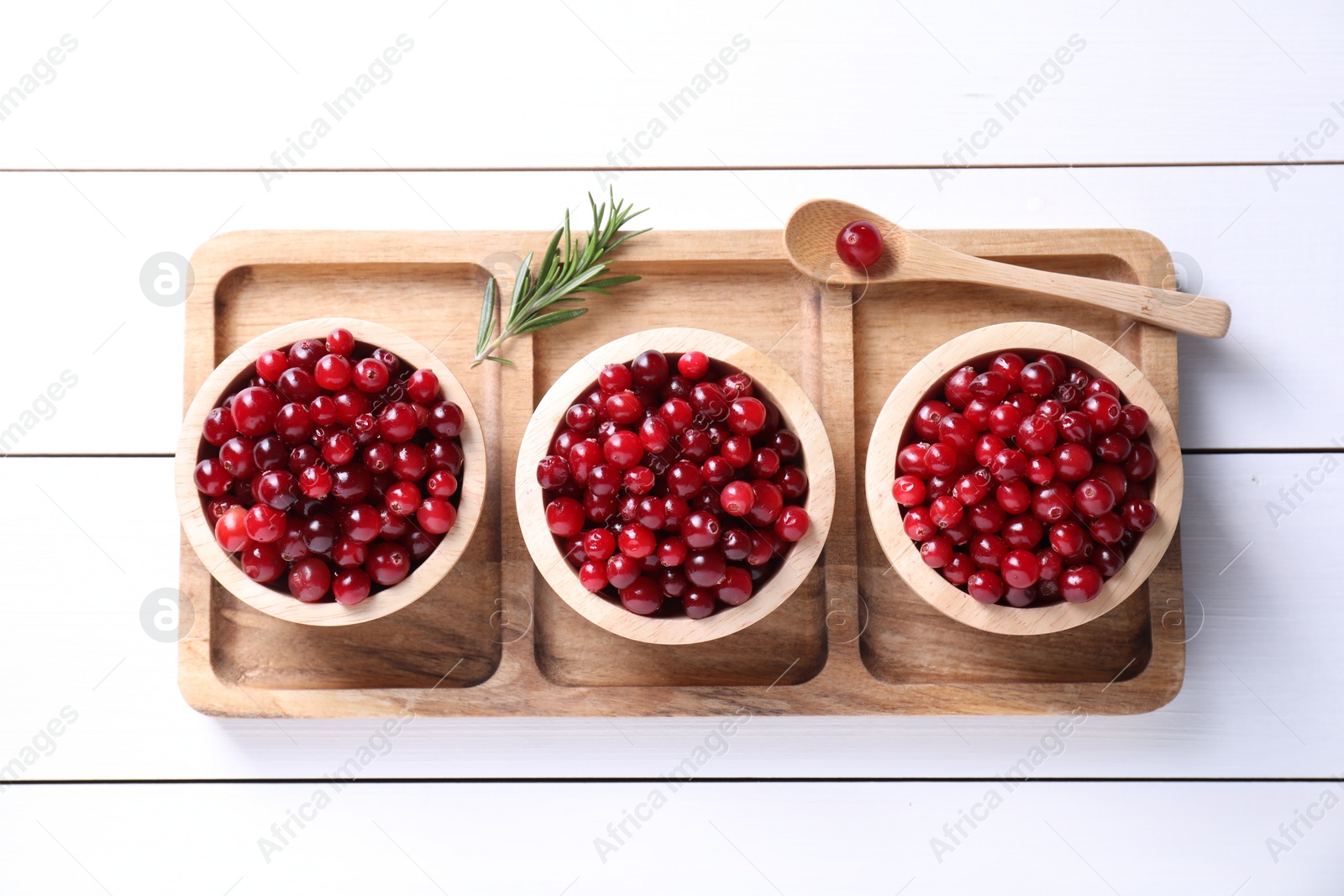 Photo of Fresh ripe cranberries in bowls and rosemary on white wooden table, top view