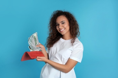 African-American woman with money in wallet on color background