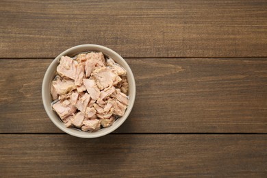 Photo of Bowl with canned tuna on wooden table, top view. Space for text