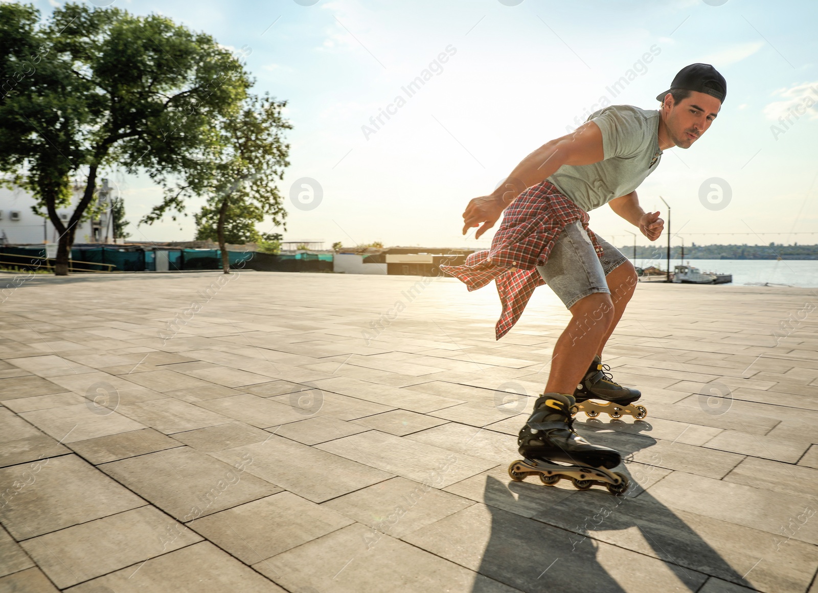 Photo of Handsome young man roller skating on pier near river, space for text