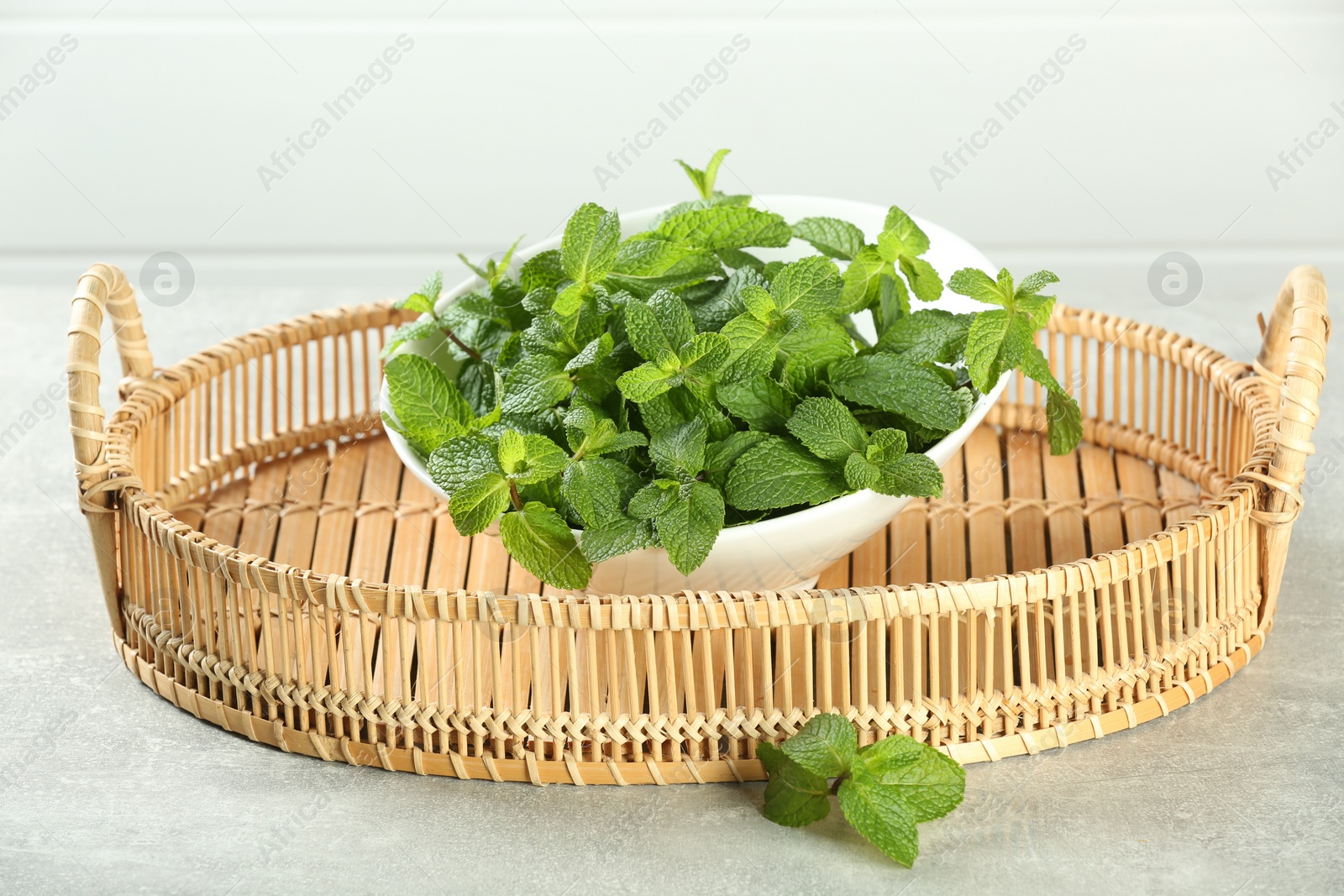 Photo of Wicker tray with bowl of fresh green mint leaves on grey table
