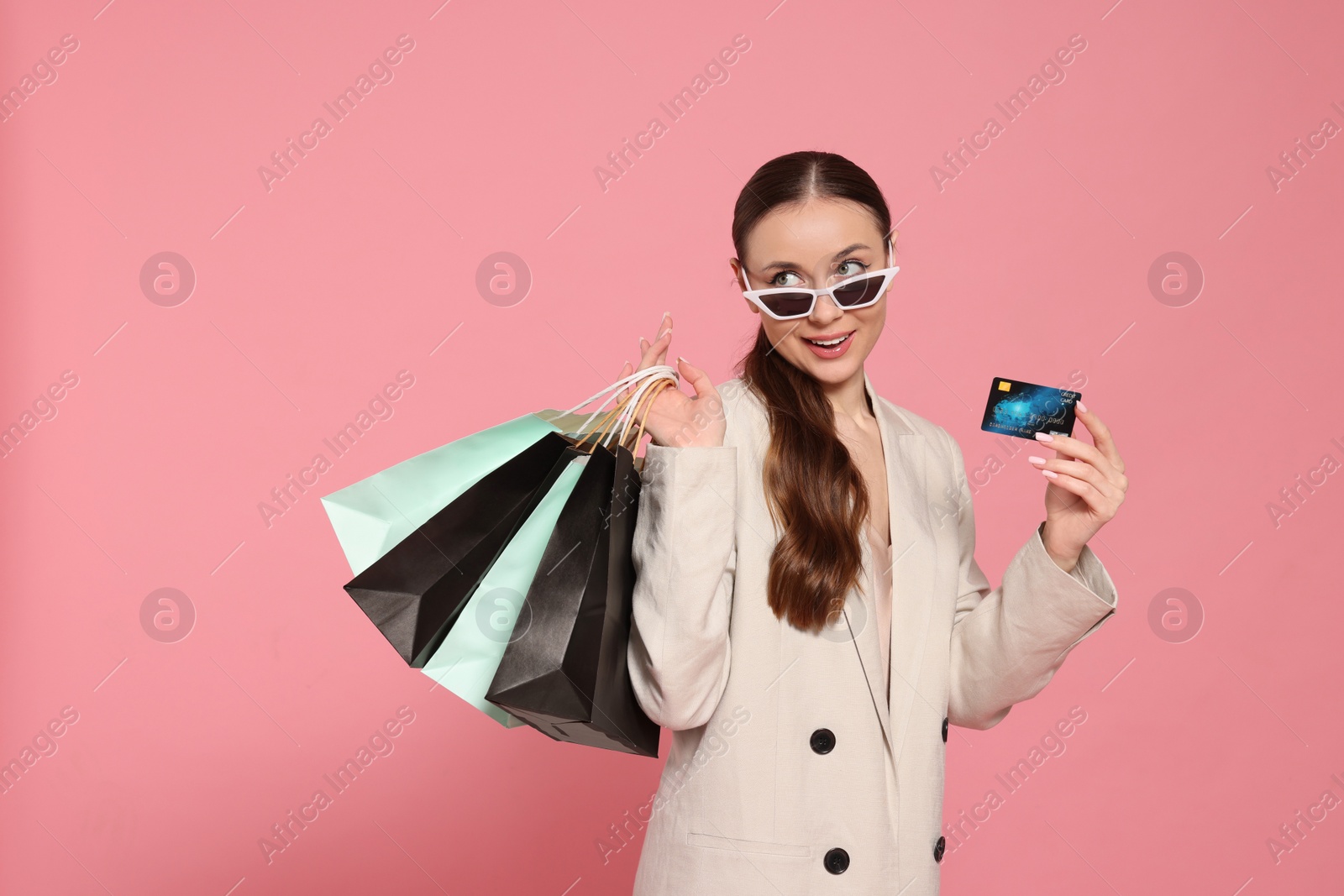 Photo of Stylish young woman with shopping bags and credit card on pink background