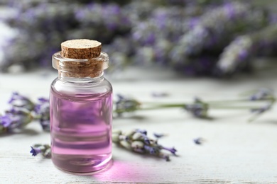 Bottle with essential oil and lavender flowers on white wooden table. Space for text