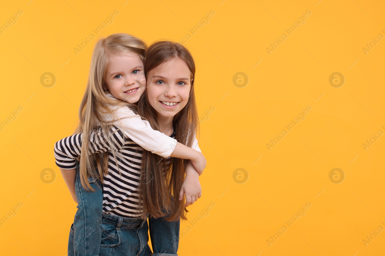 Photo of Portrait of cute little sisters on orange background, space for text