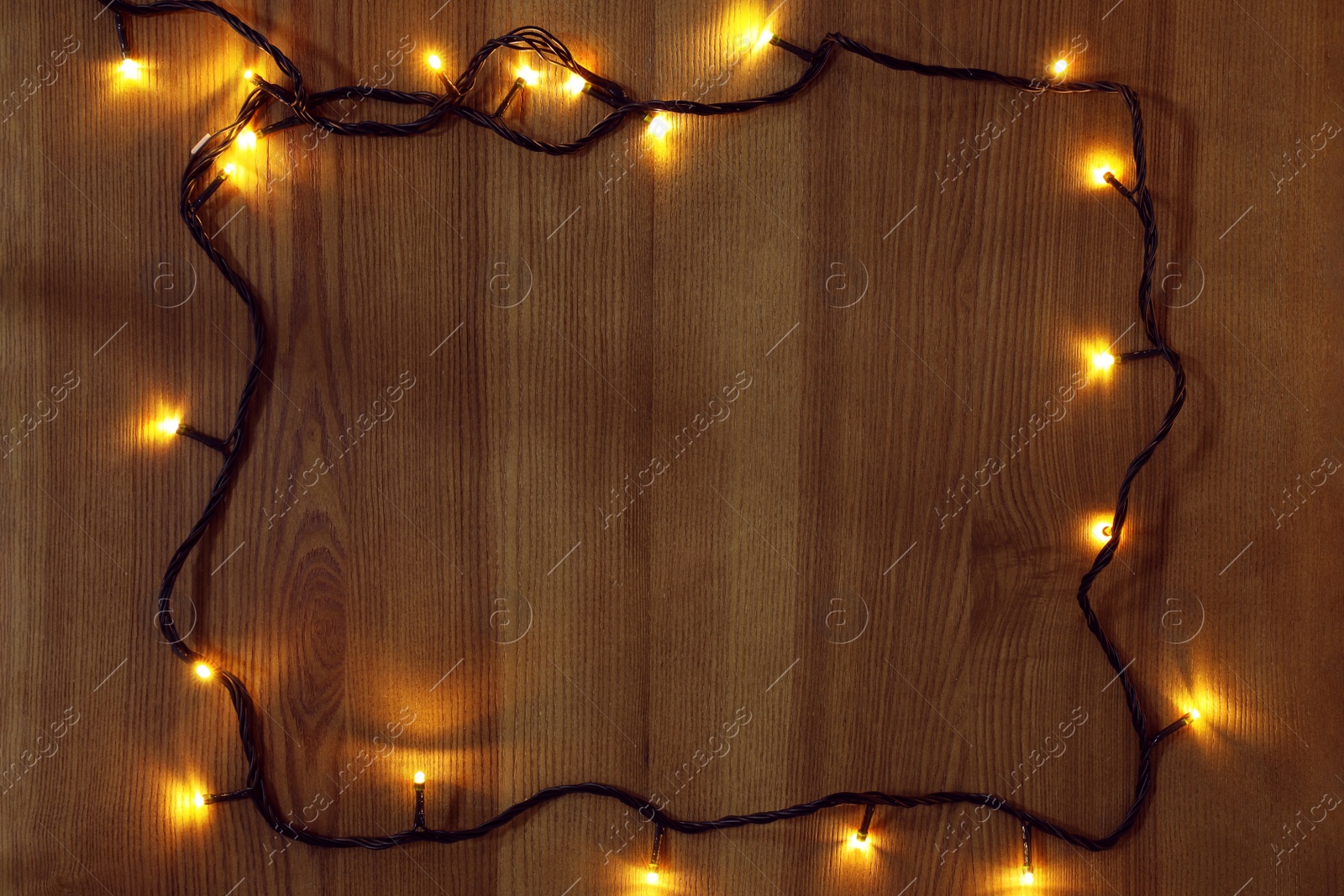 Photo of Frame of bright Christmas lights on wooden background, flat lay. Space for text