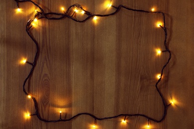 Frame of bright Christmas lights on wooden background, flat lay. Space for text