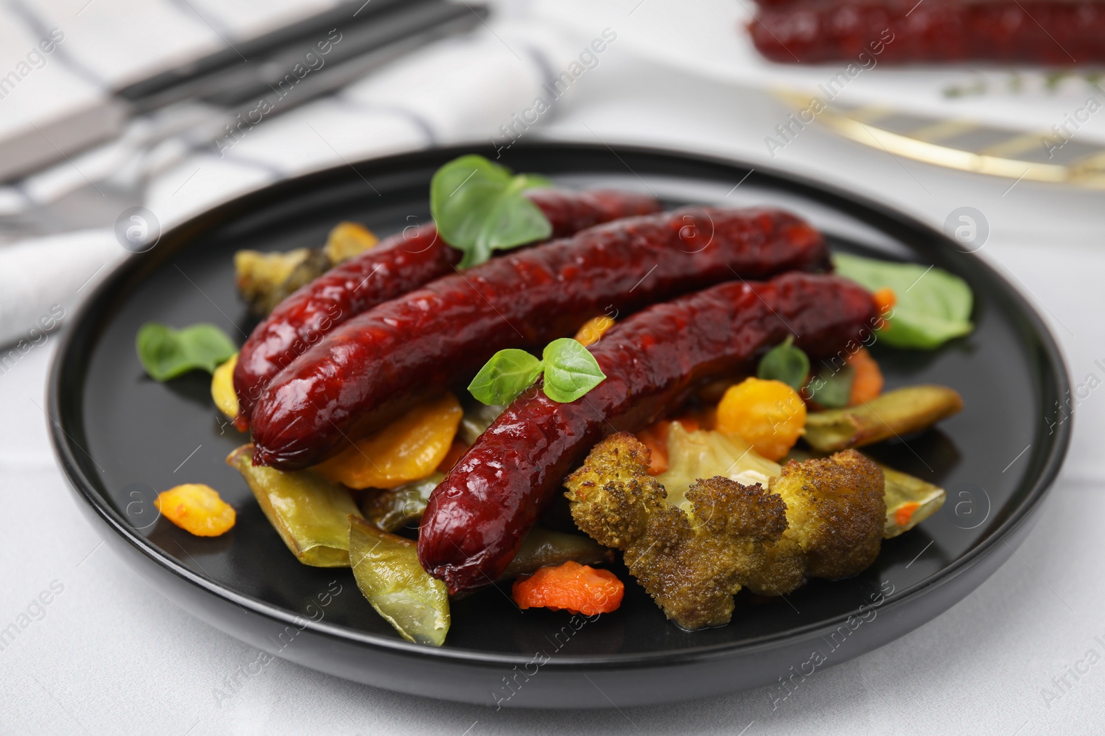 Photo of Delicious smoked sausages and baked vegetables on light table, closeup