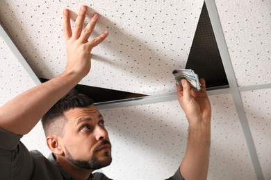 Photo of Man hiding money under ceiling cell indoors. Financial savings
