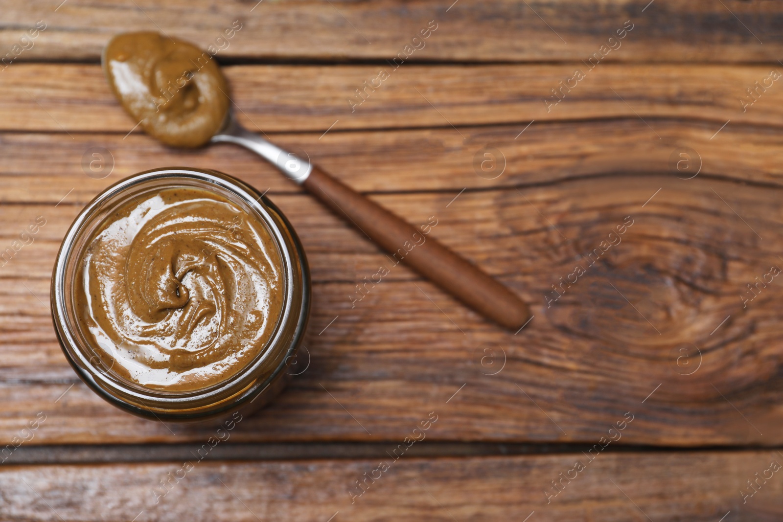 Photo of Tasty nut paste in jar and spoon on wooden table, flat lay. Space for text