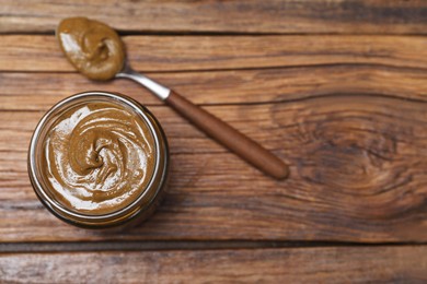 Tasty nut paste in jar and spoon on wooden table, flat lay. Space for text